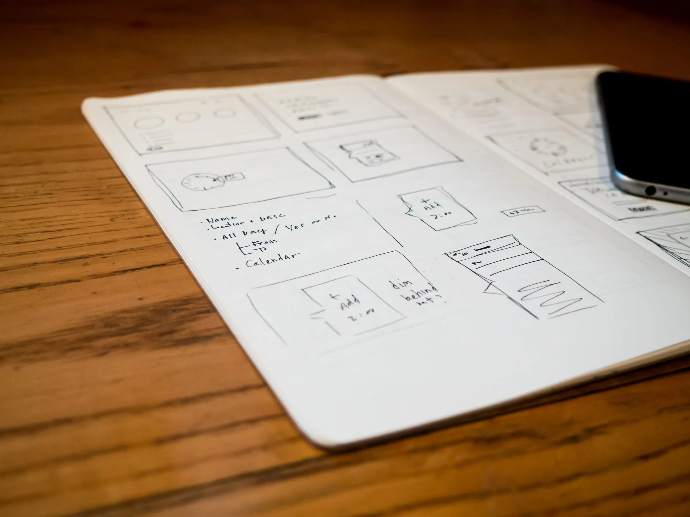 Hand-drawn website wireframes in an open notebook beside a phone