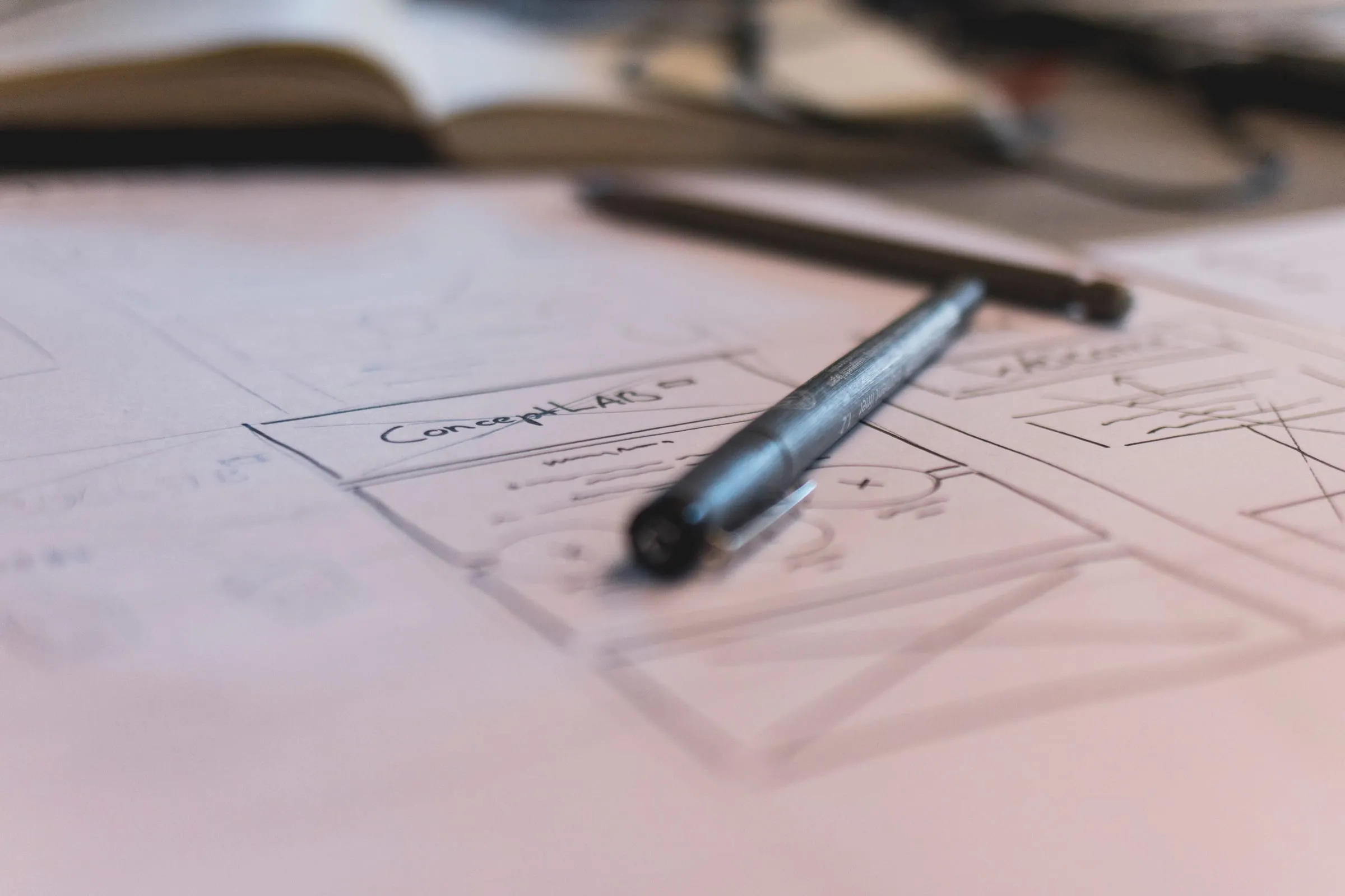 Hand-drawn website wireframes on paper with a pen resting on top